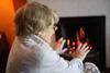 Pensioner warming herself in front of a fire