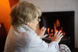 Pensioner warming herself in front of a fire