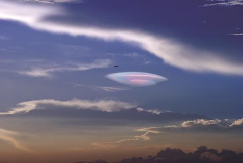 Suihkukone lentää värikkään ufonmuotoisen pilven ohi taivaalla Xiamenin kaupungin yllä Kiinassa.